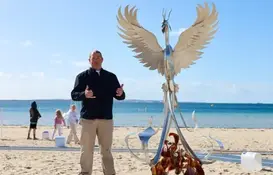 a man standing in front of a statue of a bird on a beach